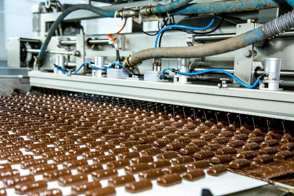 Rows of chocolate-coated sweets moving along a conveyor belt on a factory production line