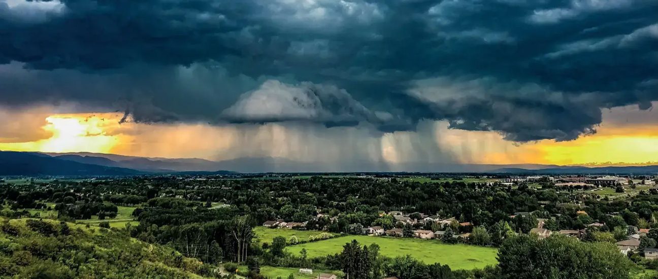 Dark storm clouds releasing heavy rain over a countryside town at sunset