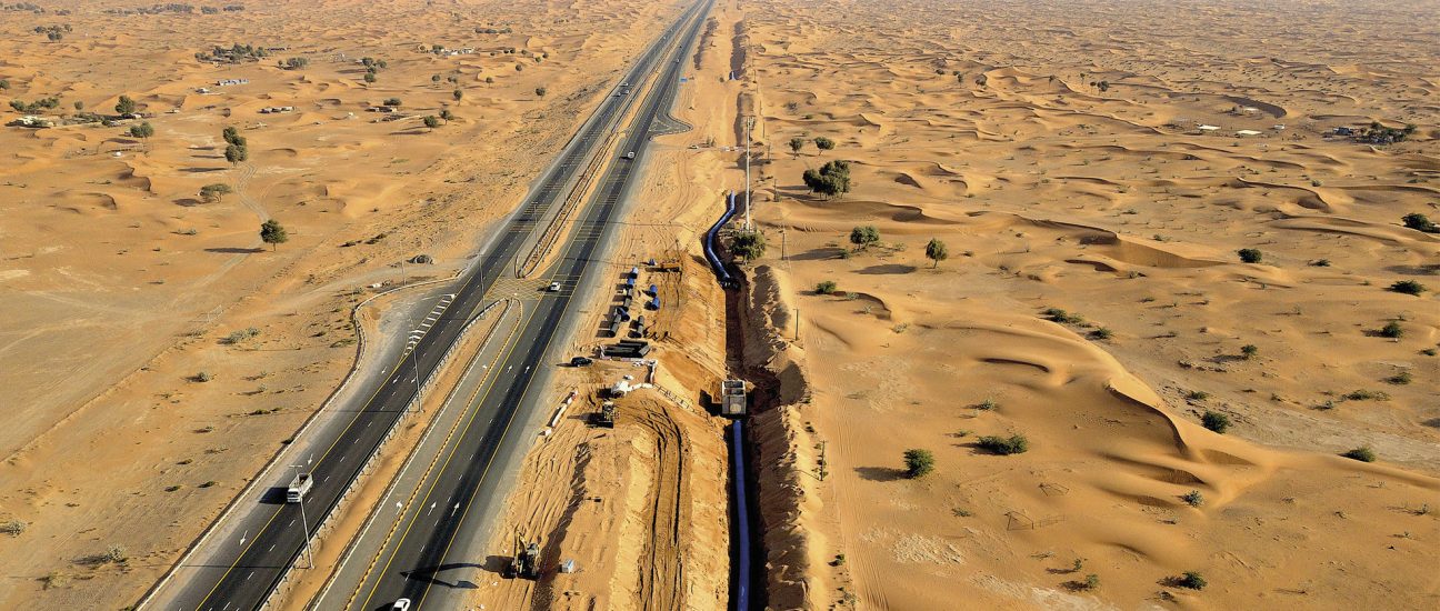 Aerial view of a highway stretching through a desert, with pipeline construction work alongside the road