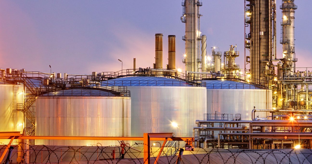 Illuminated oil refinery with large storage tanks and tall distillation towers at dusk