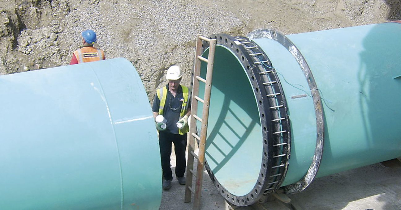 Construction workers installing large teal pipes at an excavation site
