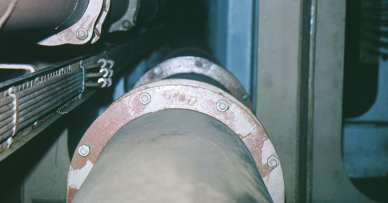 Large industrial pipes with bolted flanges running alongside a cable tray