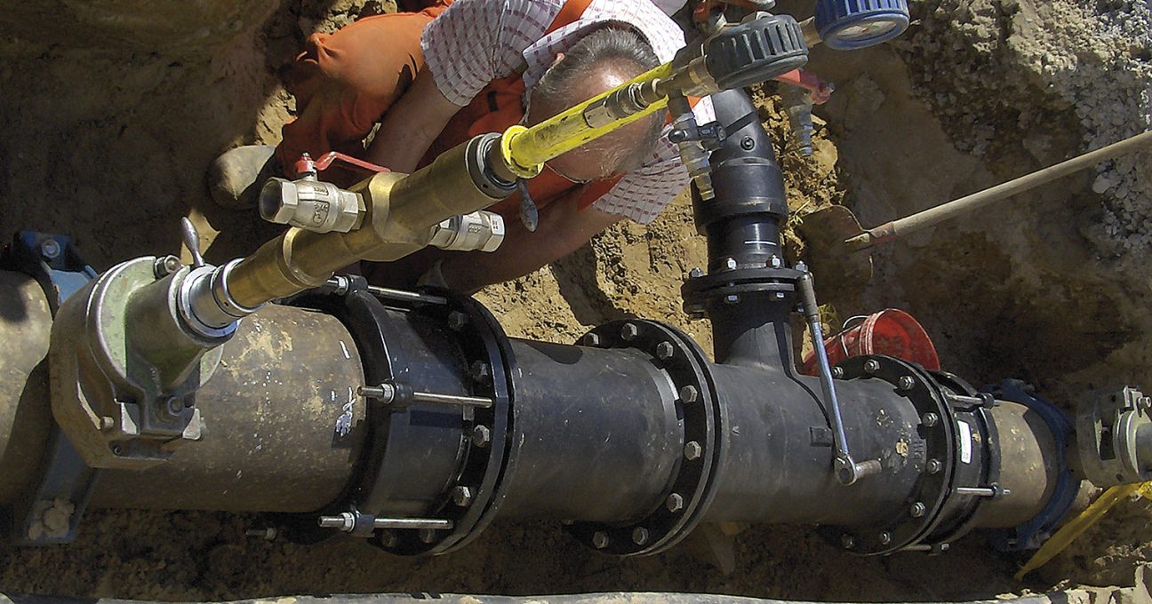 A technician installing large underground pipework and valves in a trench