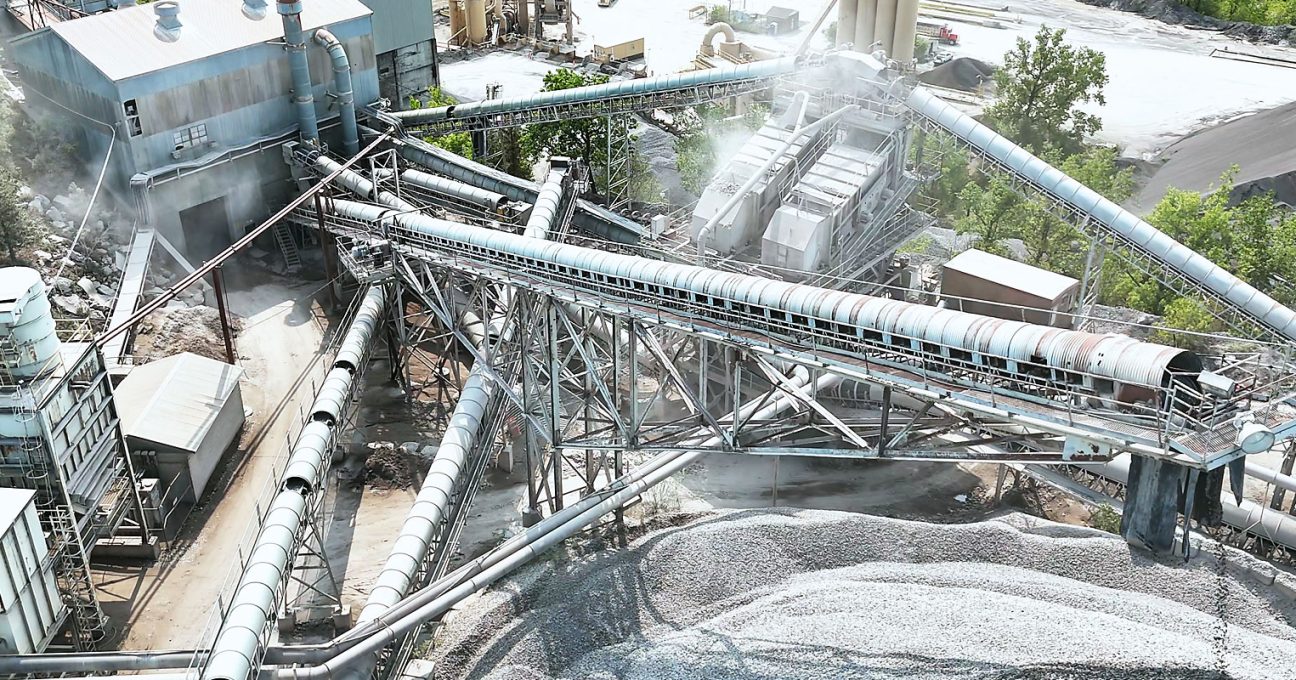 Aerial view of an industrial aggregate processing plant with elevated conveyor belts, machinery, and gravel piles