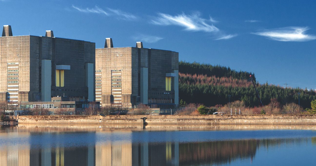 Brutalist concrete buildings of Trawsfynydd power station reflected in a lake against forested hills