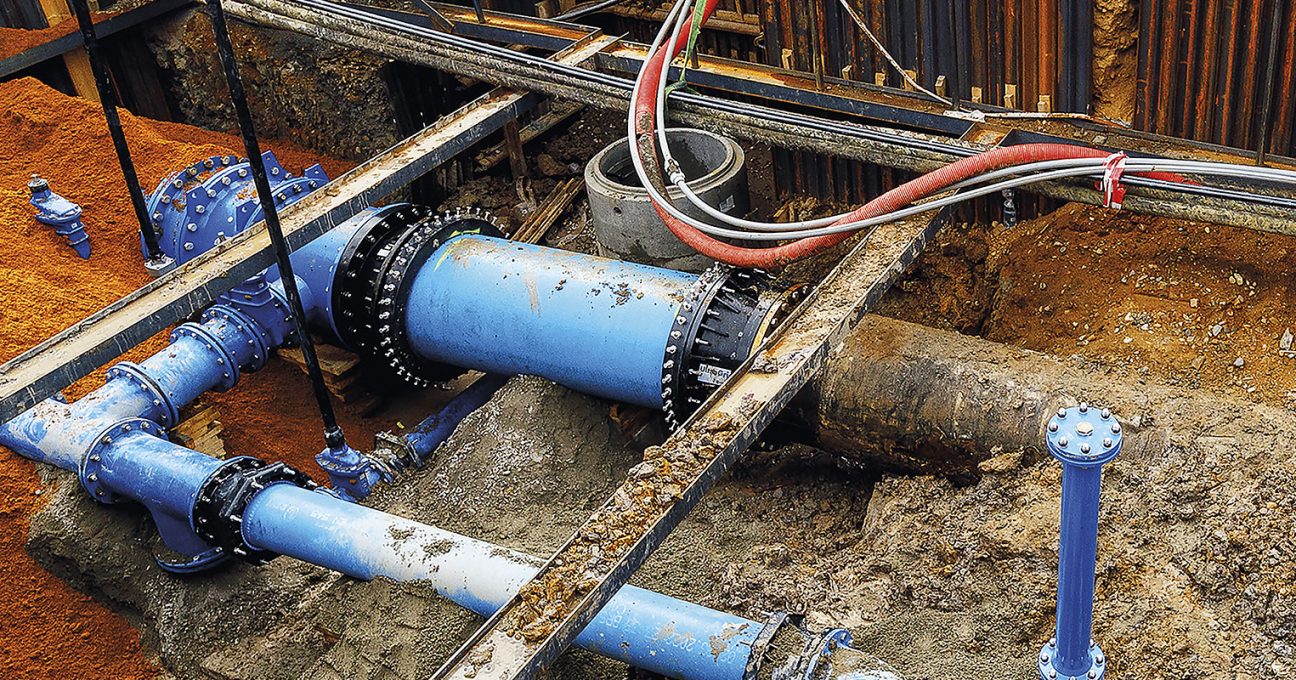 Large blue water pipes and flanged valves connected inside an excavated construction trench