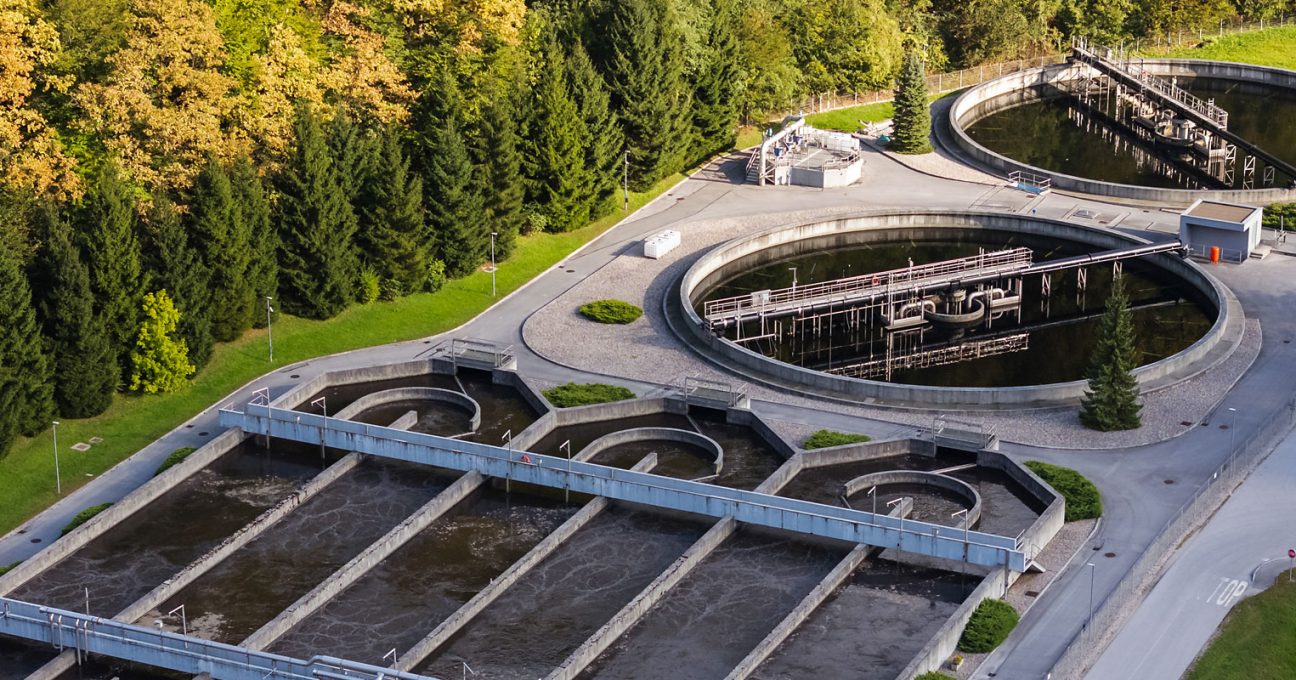 Aerial view of a wastewater treatment plant featuring large circular clarification tanks and rectangular basins