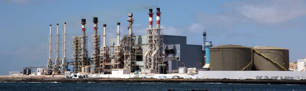 An industrial power station with tall smokestacks and large storage tanks along the coastline