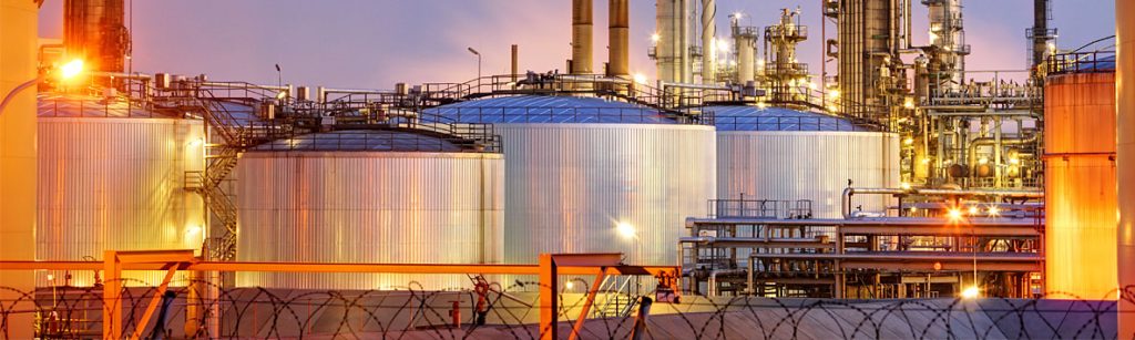 An illuminated oil refinery with large storage tanks and complex pipework at dusk