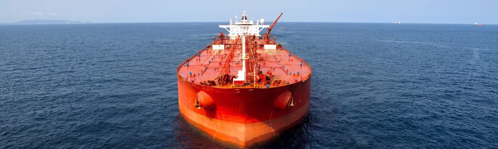 Front-facing aerial view of a large red oil tanker navigating calm blue ocean waters
