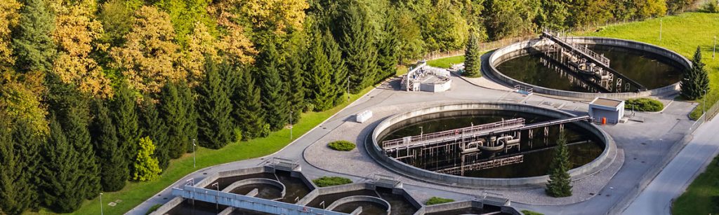 Aerial view of circular clarifier tanks at a wastewater treatment facility next to a forest