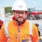A man wearing a white hard hat, glasses, and a Wessex Water high-visibility jacket at a construction site