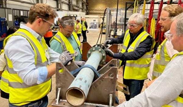 Engineers wearing high-visibility vests and safety glasses examining a large pipe in an industrial workshop