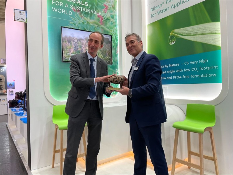Two men in suits holding an award trophy together at an exhibition stand
