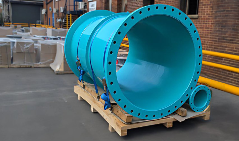 Large turquoise flanged pipes secured to a wooden pallet outside a warehouse