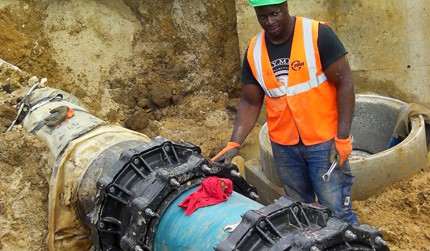 A construction worker in a high-visibility vest and hard hat working on a large underground pipe in a trench
