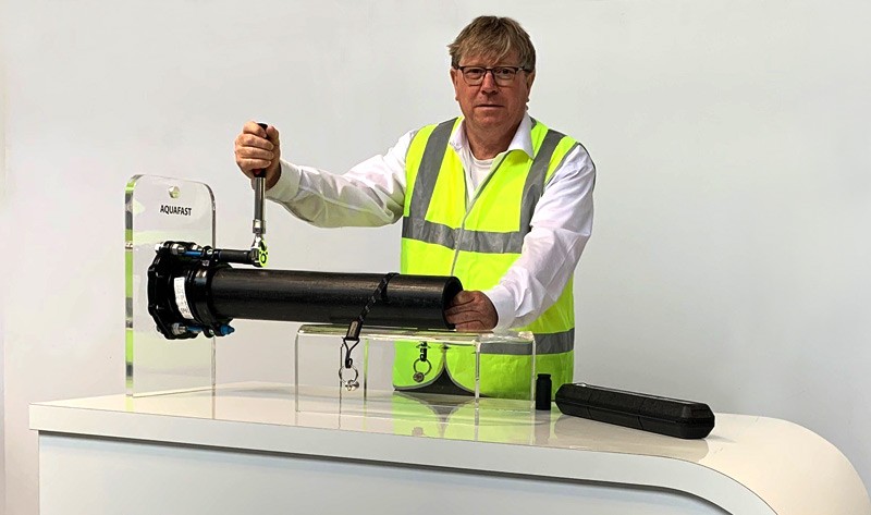 A man wearing a high-visibility vest uses a torque wrench on an Aquafast pipe coupling display