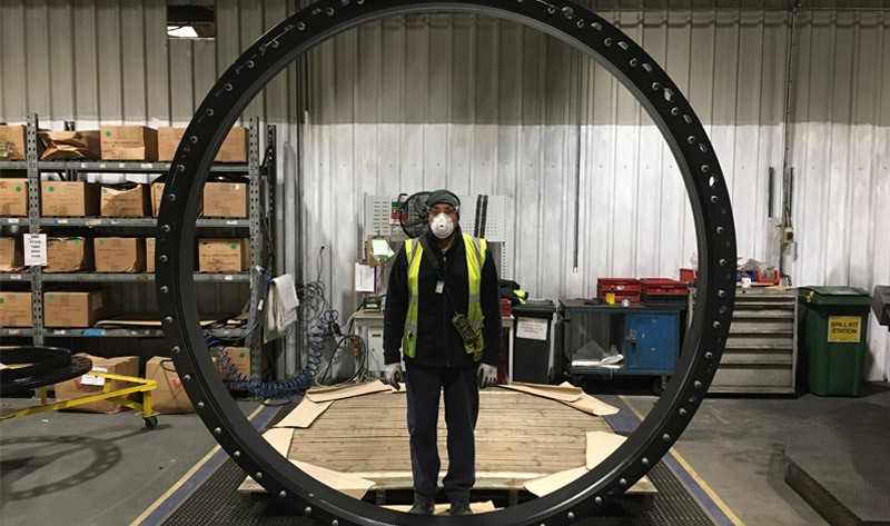 A factory worker in safety gear standing inside a massive circular metal component to show its scale
