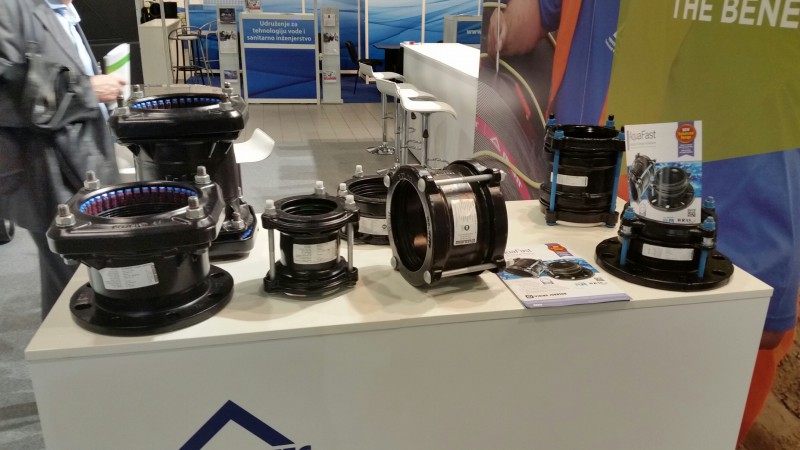 Various black industrial pipe couplings, flange adaptors, and product brochures on display at a trade show stand