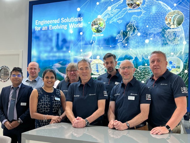 A group of eight team members standing in front of a large digital display showing a globe graphic