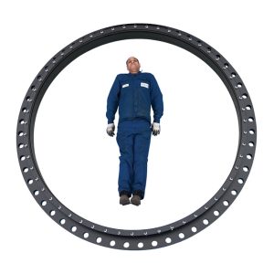 A man in blue overalls standing inside a large industrial slewing bearing ring to demonstrate its scale