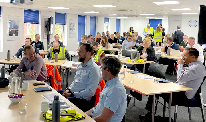 Attendees sitting at tables in a bright office training room during a presentation