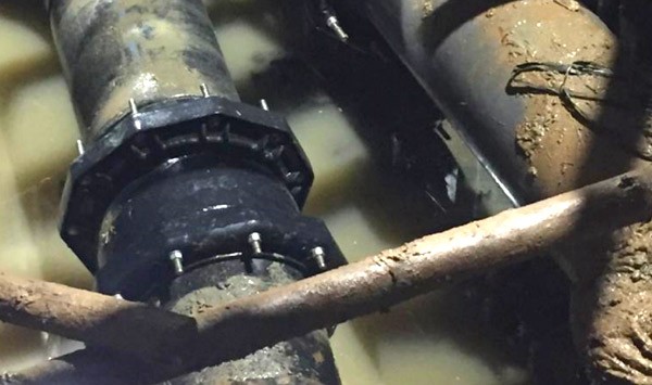 A bolted black pipe coupling submerged in muddy water