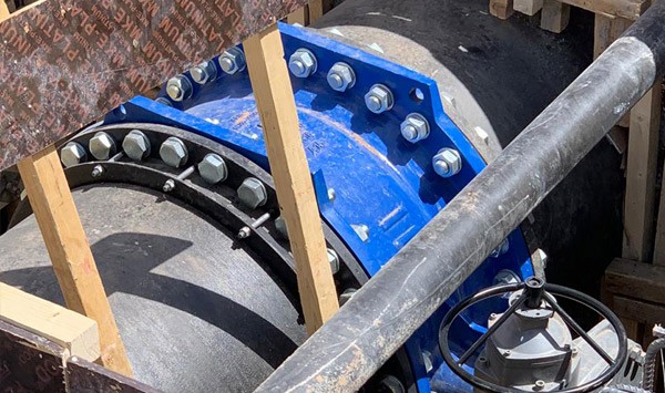 Large black pipe fitted with a blue bolted flange coupling and control valve in a trench