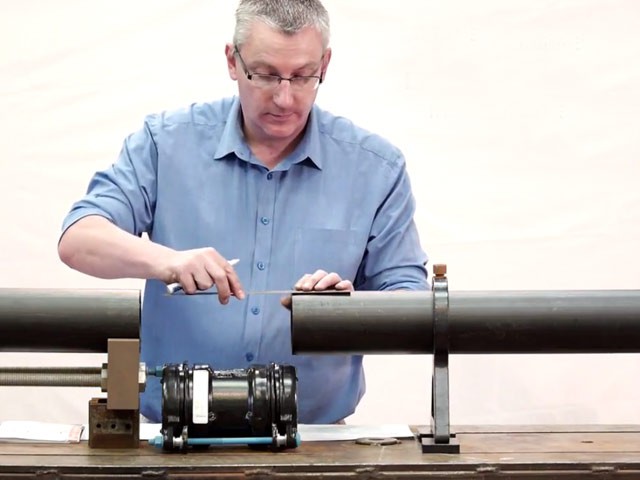 A man using a ruler and marker to measure and mark a black pipe on a workbench