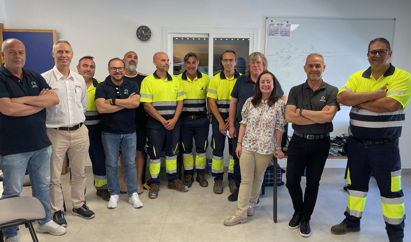 Group of twelve team members, including office staff and workers in high-visibility uniforms, posing together indoors