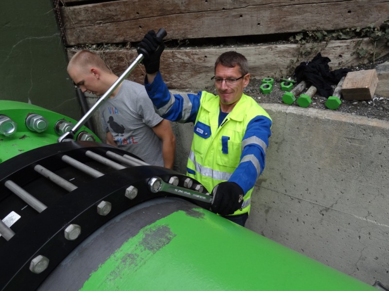 Two workers using spanners to tighten bolts on a large green industrial pipe flange