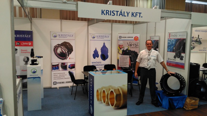A representative standing at the Kristály Kft. trade fair stand displaying pipe couplings and industrial valves
