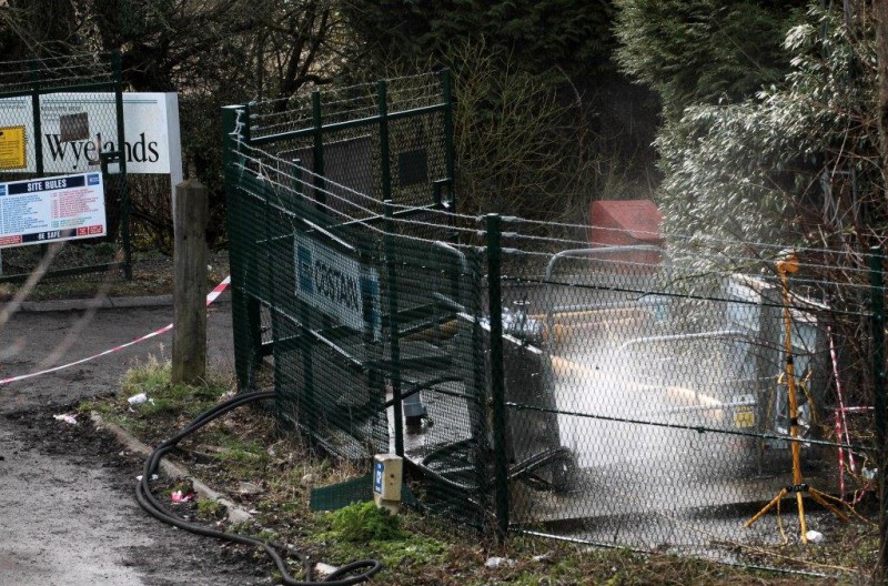 Water spraying forcefully from behind a green security fence near a sign for Wyelands