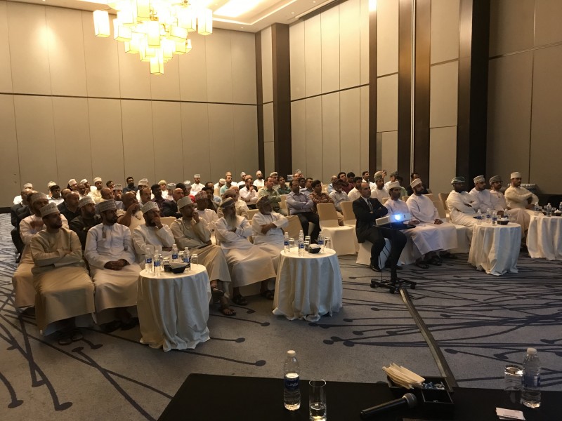 Audience members, many in traditional Omani attire, seated in a conference hall watching a presentation
