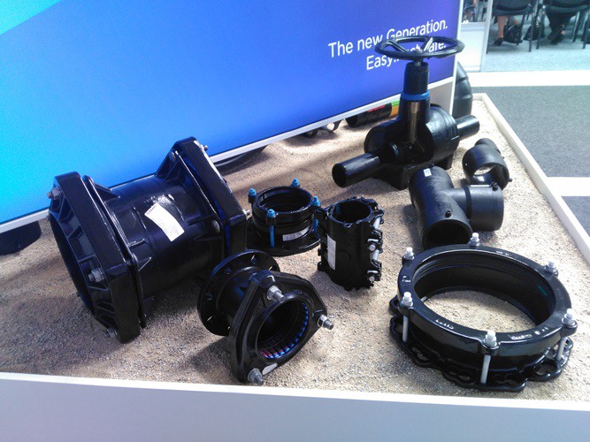Display of black industrial pipe fittings, couplings, and a valve on a bed of sand
