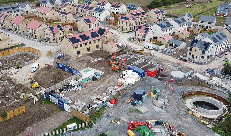 Aerial view of a modern housing development under construction, with solar panels on house roofs and active diggers