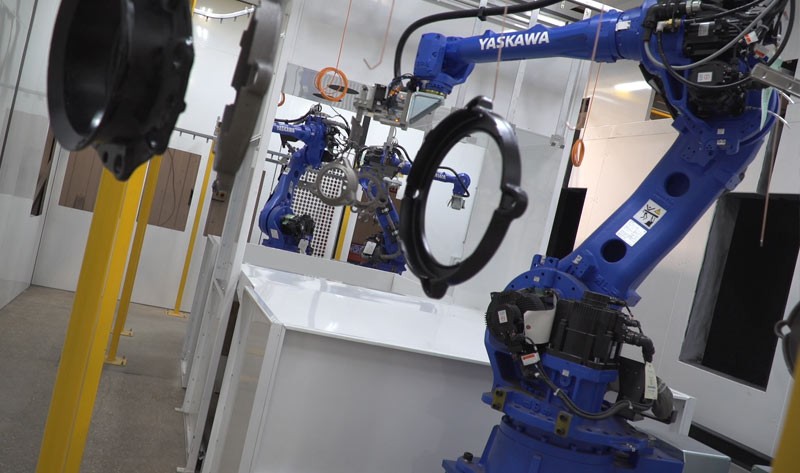 Blue robotic arms operating along an automated industrial assembly line with suspended metal components