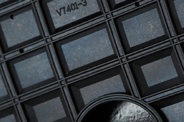 Close-up of a black grid-patterned surface stamped with text V7401-3