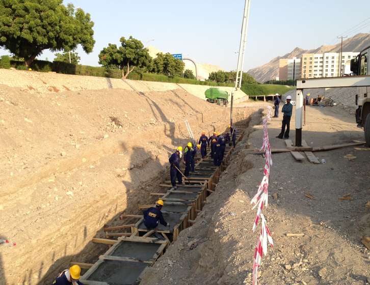 Construction workers wearing hard hats pouring concrete into wooden formwork inside a trench