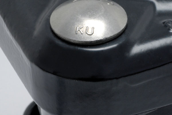 Silver metal rivet stamped with the letters KU on a dark grey surface