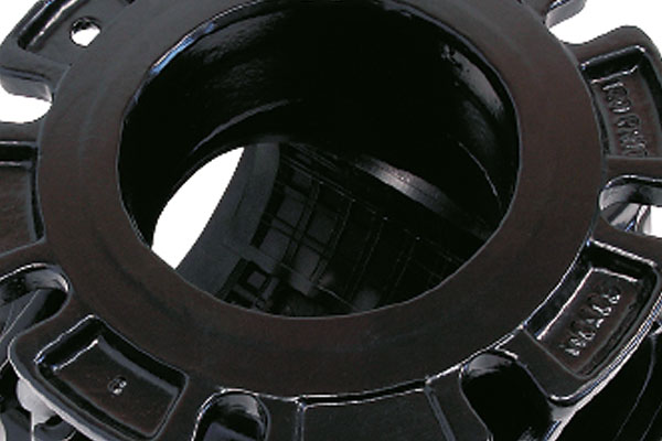 Close-up of a black cast iron pipe flange with notched bolt holes around the outer rim