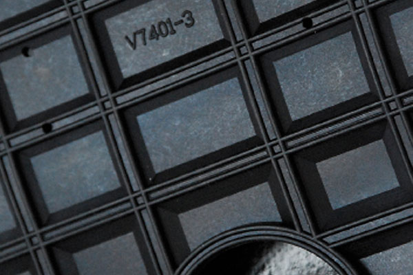 Close-up of a dark textured grid pattern with recessed rectangular panels stamped with V7401-3