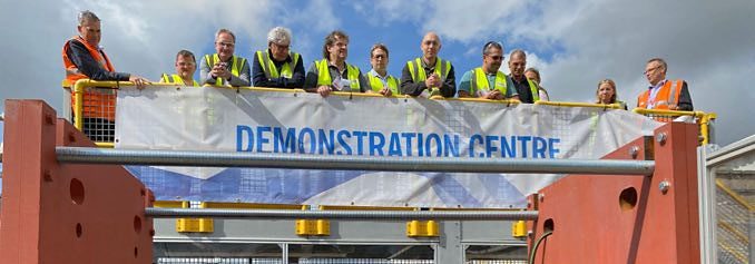 Group of people in high-visibility vests standing on a platform behind a banner reading Demonstration Centre