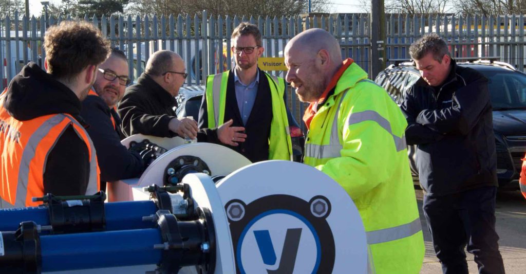 Workers wearing hi-vis jackets gathered around industrial equipment outdoors