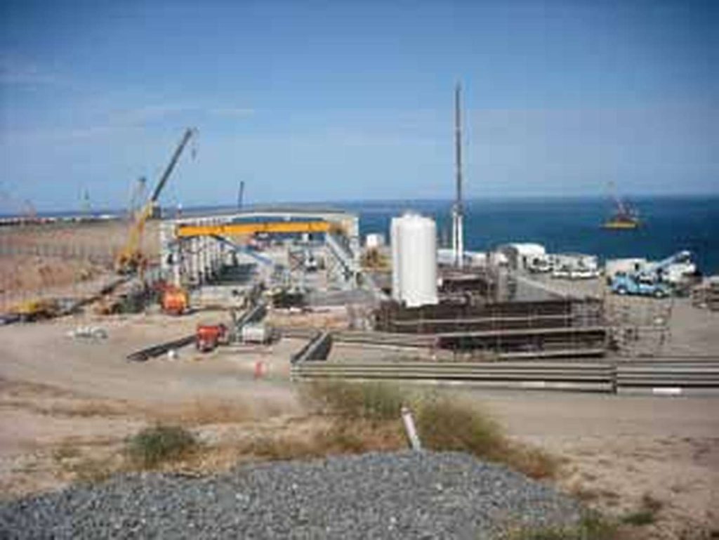 Industrial construction site along the coast with cranes, storage tanks and building framework