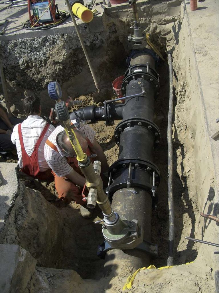 Two workers in a trench installing and pressure-testing large underground piping
