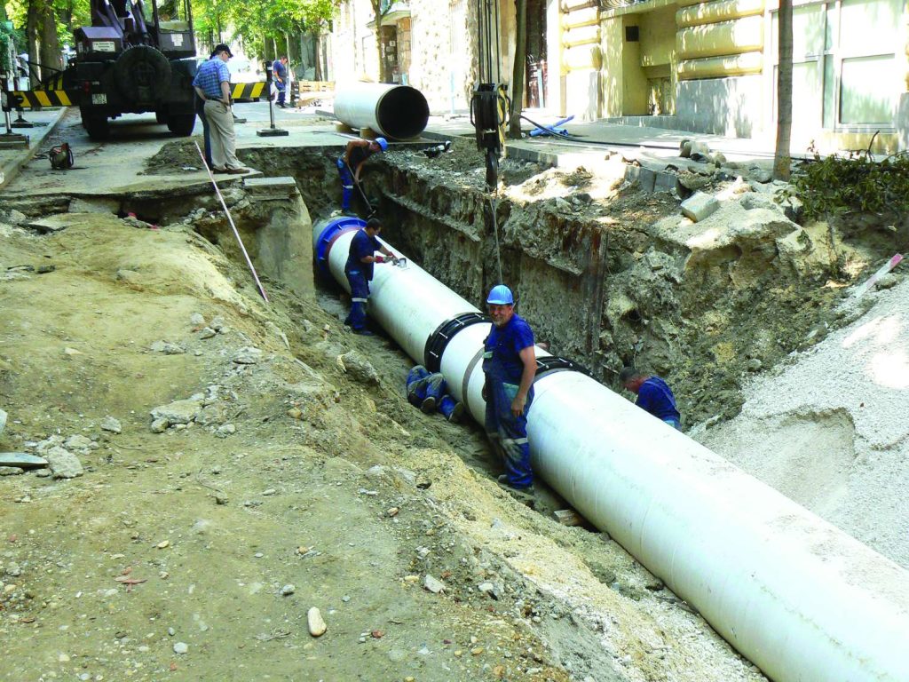 Construction workers installing a large white pipe in a trench along a street