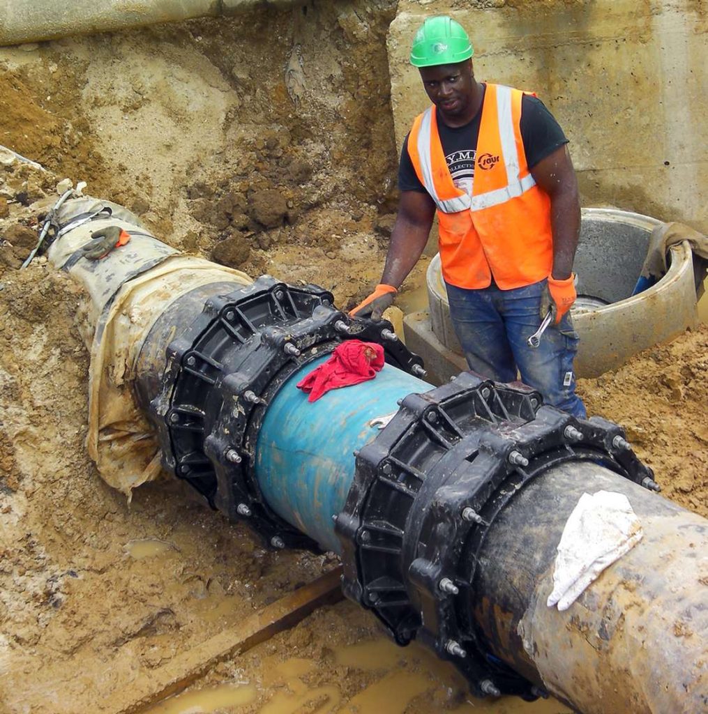 Construction worker in a green hard hat and hi-vis vest standing in a trench next to a large pipe joint