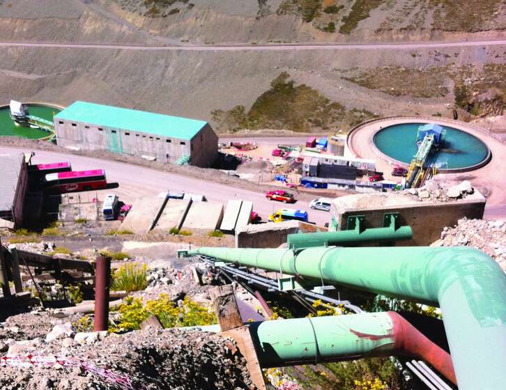 High-angle view of a mountain mining facility with large green pipelines, circular settling ponds, and industrial buildings