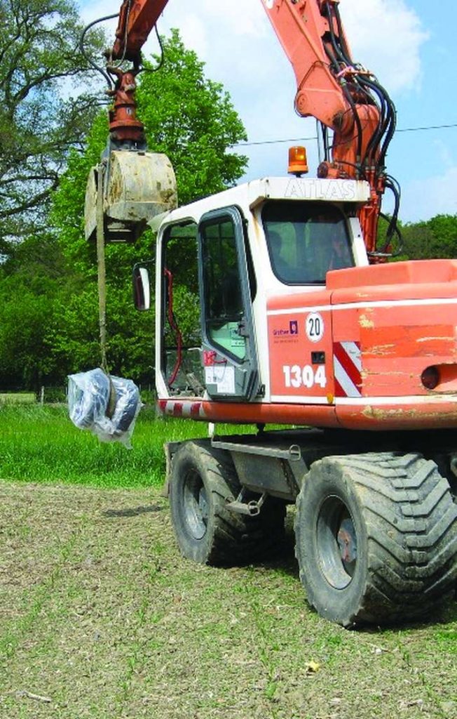 An orange Atlas wheeled excavator lifting a wrapped load using a strap attached to its grab bucket